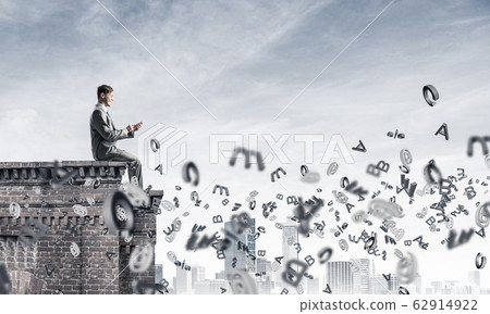 Man on roof edge send message with smartphone and symbols flying Man on roof edge send message with smartphone and symbols flying 62914922
