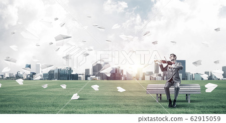 Handsome violinist in park on wooden bench play his melody Handsome violinist in park on wooden bench play his melody 62915059