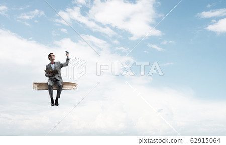 Young businessman or student floating in blue sky and studying the science 62915064