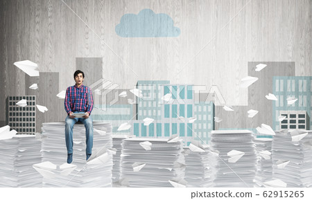 Young man sitting on pile of paper documents. Young man sitting on pile of paper documents. 62915265