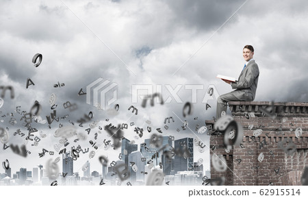 Man on roof edge reading book and symbols flying around Man on roof edge reading book and symbols flying around 62915514