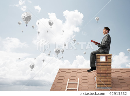 Man on roof reading book and aerostats flying in air 62915882