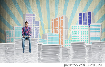 Young man sitting on pile of paper documents. Young man sitting on pile of paper documents. 62916151