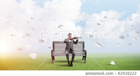 Handsome violinist in park on wooden bench play his melody 62916222