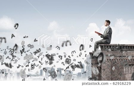 Man on roof edge reading book and symbols flying around Man on roof edge reading book and symbols flying around 62916229
