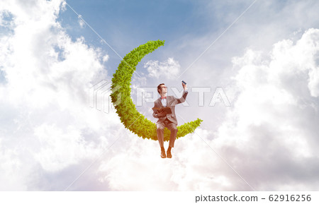 Young businessman or student on moon in sky studying the science Young businessman or student on moon in sky studying the science 62916256