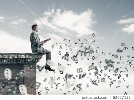Man on roof edge reading book and symbols flying around Man on roof edge reading book and symbols flying around 62917121