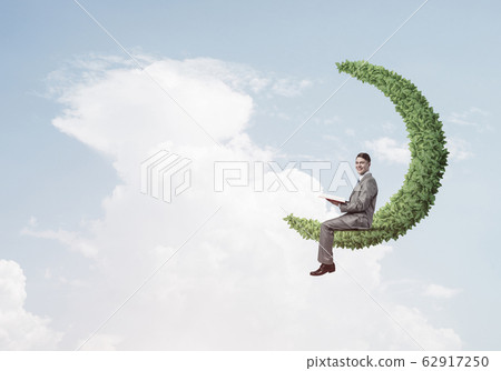 Businessman or student sitting on green moon and reading book 62917250