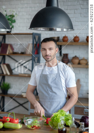 Young guy in an apron preparing vegetable food. 62922158