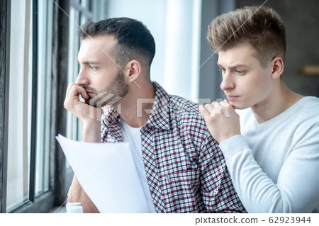 Two young men standing near the window looking desperate 62923944