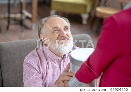 Grey-haired bearded man looking happy taking a gift from his wife 62924400