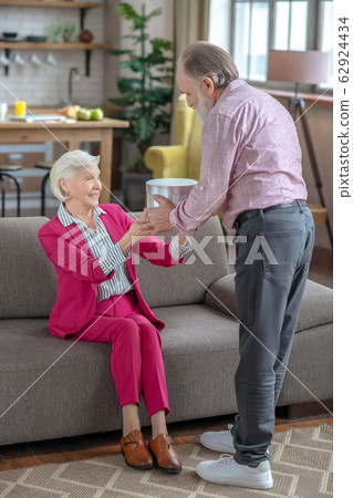 Grey-haired elderly lady in bordeaux suit taking a gift 62924434