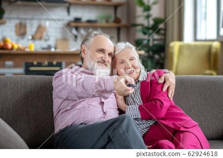 Man in a pink shirt hugging his wife while turning on tv 62924618