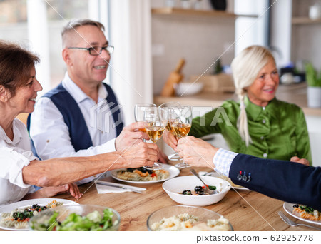 Group of senior friends at dinner party at home, clinking glasses. 62925778