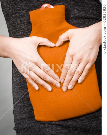 Girl holds hot water bottle on belly making heart 62925926