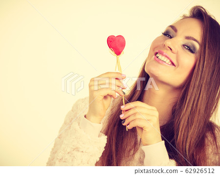Flirty woman holding red wooden heart on stick Flirty woman holding red wooden heart on stick 62926512