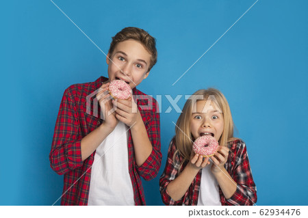Unhealthy Sweets. Preteen Brother And Sister Eating Donuts On Blue Background Unhealthy Sweets. Preteen Brother And Sister Eating Donuts On Blue Background 62934476