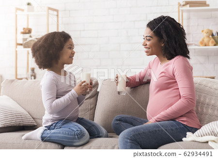 Pregnant afro mom and cute little daughter drinking milk at home Pregnant afro mom and cute little daughter drinking milk at home 62934491