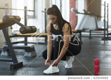 Pretty young woman tying shoelaces in sports club Pretty young woman tying shoelaces in sports club 62934492
