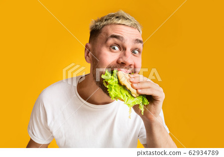 Funny guy eating a burger, eyes wide open 62934789