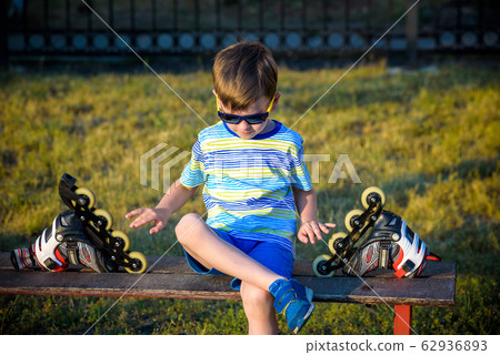 Little handsome boy in roller-blades sits in bench Little handsome boy in roller-blades sits in bench 62936893