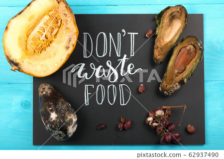 Close up of a chalkboard with Don't waste food lettering and rotten fruits. Selective focus. 62937490