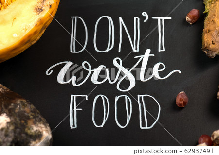 Close up of a chalkboard with Don't waste food lettering and rotten fruits. Selective focus. Close up of a chalkboard with Don't waste food lettering and rotten fruits. Selective focus. 62937491