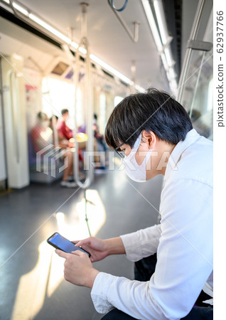 Asian man wearing mask using phone on skytrain Asian man wearing mask using phone on skytrain 62937766