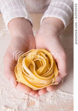 A young woman is holding fresh homemade pasta - Italian tagliatelle. Italian pasta made from flour, water and eggs. A young woman is holding fresh homemade pasta - Italian tagliatelle. Italian pasta made from flour, water and eggs. 62939350