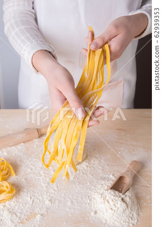 A young woman is holding fresh homemade pasta - Italian tagliatelle. Italian pasta made from flour, water and eggs. 62939353