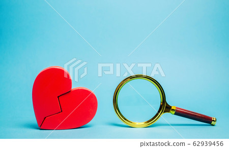 Red heart and a magnifying glass. The concept of finding love and relationships. Find a soul mate. Loneliness. Family psychologist services. Valentine's Day. 62939456