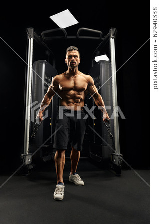 Muscular bodybuilder doing crossover cable exercise. Muscular bodybuilder doing crossover cable exercise. 62940338