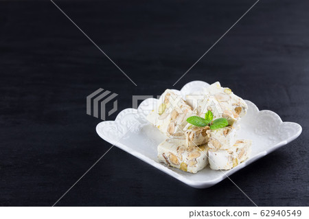 Italian torrone or nougat with almonds and pistachios from Apulia, traditional christmas sweets on black background 62940549