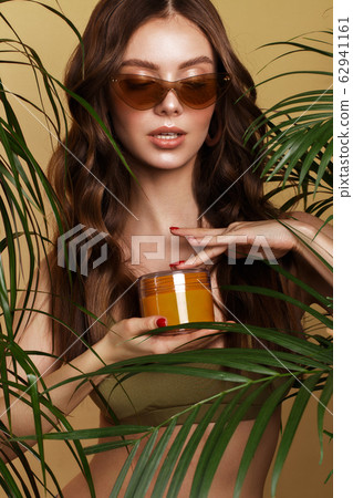 Beautiful sexy woman in a bikini posing in the middle of green plants with a box of cosmetics in hand. Summer look. Beauty face Beautiful sexy woman in a bikini posing in the middle of green plants with a box of cosmetics in hand. Summer look. Beauty face 62941161
