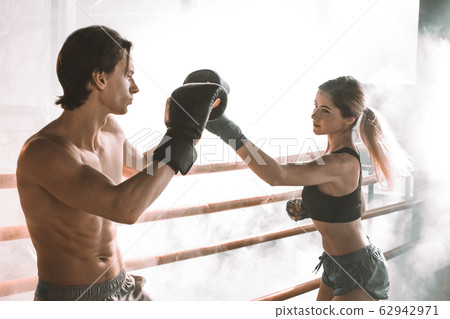 Boxing workout. Couple man and woman boxing together in the boxing ring at the gym. Sport box exercise two people. Man trainer in boxing gloves, woman in boxing bandages. 62942971
