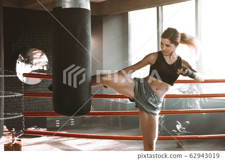 Young woman trains in boxing ring with heavy..