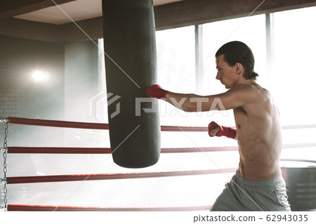 angry boxer standing in boxing pose near punching bag on black with smoke angry boxer standing in boxing pose near punching bag on black with smoke 62943035