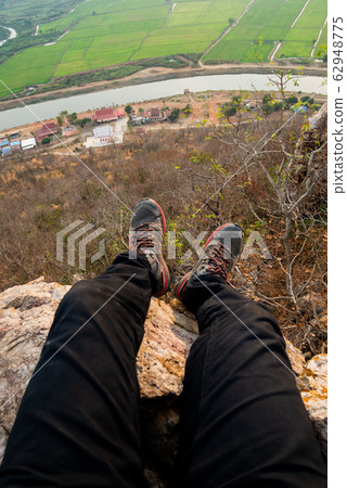 Legs of traveler sitting on  high mountain cliff 62948775