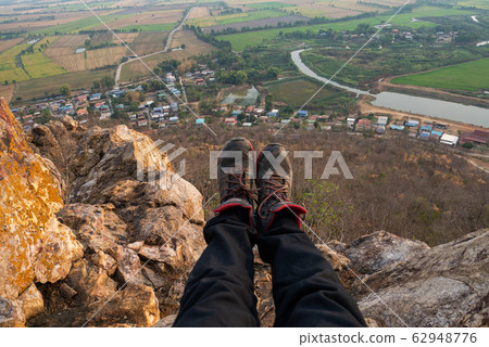 Legs of traveler sitting on  high mountain cliff 62948776