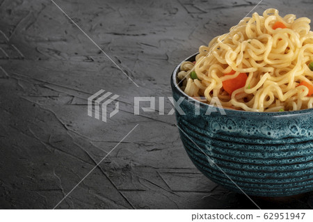 Instant noodles closeup, a bowl of soba with carrot and scallions on a black background with a place for text Instant noodles closeup, a bowl of soba with carrot and scallions on a black background with a place for text 62951947