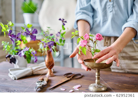 A young woman florist create flower arrangement Ikebana in kenzan. Uses scissors and pruner. Seasonal summer garden flowers. 62952361