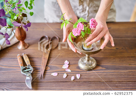 A young woman florist create flower arrangement Ikebana in kenzan. Uses scissors and pruner. Seasonal summer garden flowers. 62952375