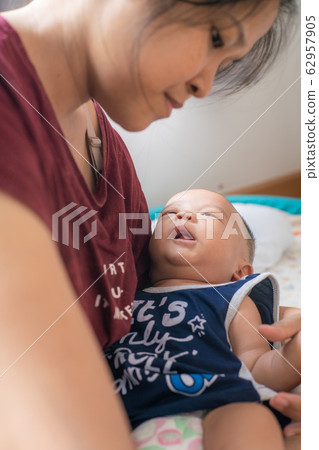 Asian women holding smiling infant boy in bedroom Asian women holding smiling infant boy in bedroom 62957905