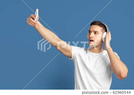 Caucasian young man's portrait on blue studio background Caucasian young man's portrait on blue studio background 62960544