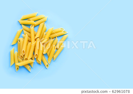 Uncooked penne pasta isolated on blue background. Uncooked penne pasta isolated on blue background. 62961078