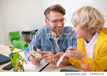 Male teacher showing boy control unit, smiling Male teacher showing boy control unit, smiling 62962545