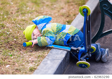 Cute little boy falling off his scooter Cute little boy falling off his scooter 62963290
