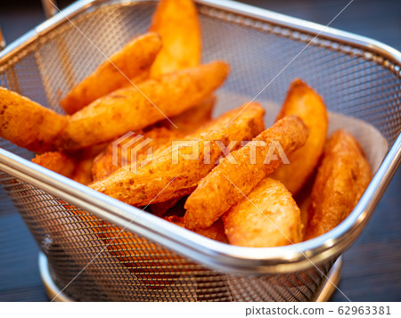 Deep-fried potato wedges. Basket of freshly made French fries close up. Deep-fried potato wedges. Basket of freshly made French fries close up. 62963381