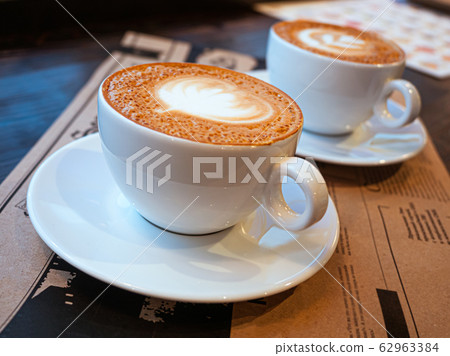 Two cups of cappuccino on a table in a cafe. drawing heart on Latte coffee froth. Delicious coffee for breakfast Two cups of cappuccino on a table in a cafe. drawing heart on Latte coffee froth. Delicious coffee for breakfast 62963384