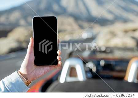 Holding phone with empty screen on the roadside Holding phone with empty screen on the roadside 62965254